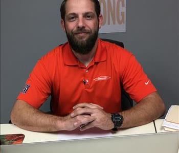 Male with orange shirt sitting at a desk.